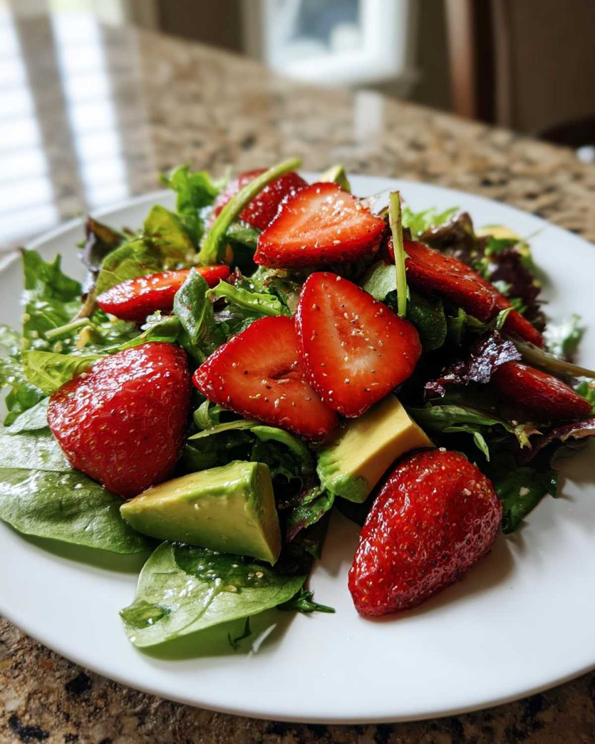 Close-up of a fresh Easy Strawberry Avocado Salad with mixed greens, sliced strawberries, and avocado chunks on a white plate.