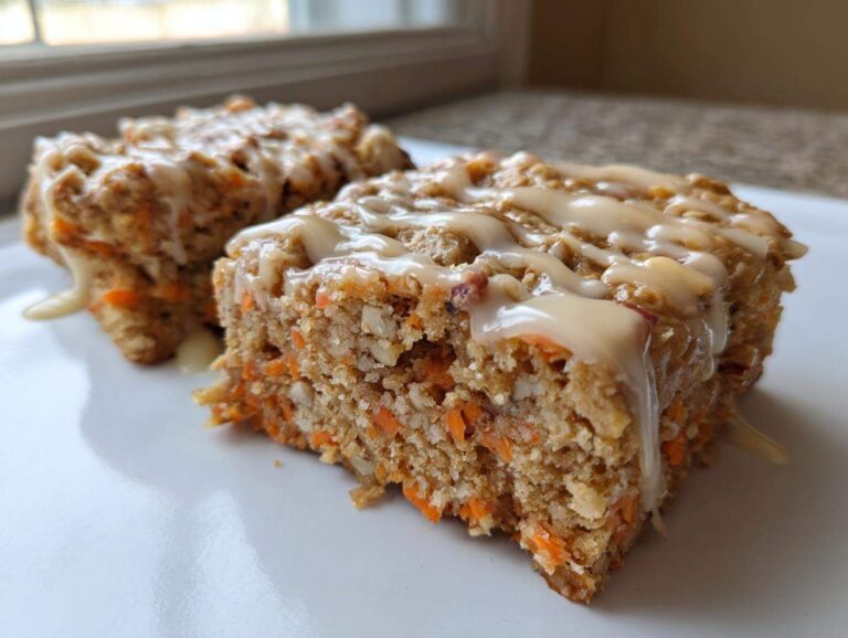 Two slices of Gluten-Free Carrot Cake Baked Oats topped with a creamy vanilla glaze, served on a white plate.