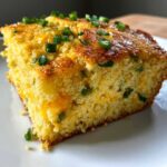 Close-up of a moist slice of Gluten-Free Cheddar Jalapeno Cornbread topped with melted cheese and green onions.