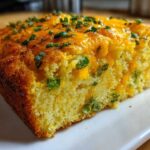 Close-up of a moist slice of Gluten-Free Cheddar Jalapeno Cornbread topped with melted cheese and fresh chives.