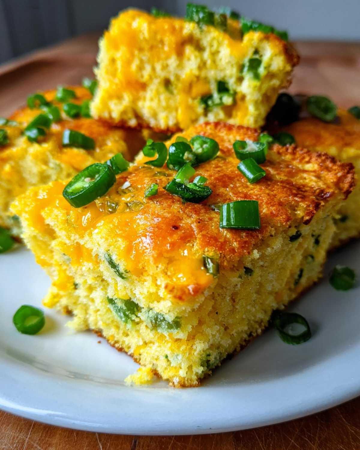 Close-up of moist Gluten-Free Cheddar Jalapeno Cornbread squares topped with melted cheese and fresh sliced green jalapeños.