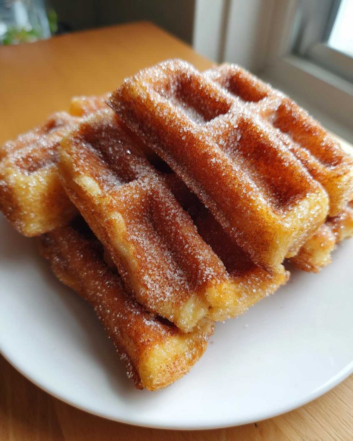 Close-up of golden Gluten-Free Cinnamon Sugar Waffle Sticks piled on a white plate, heavily coated in sparkling cinnamon sugar.