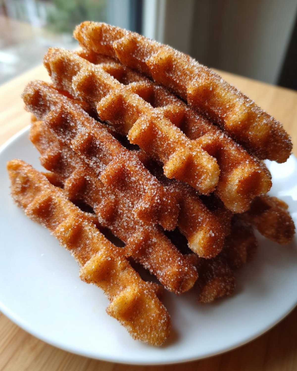 A close-up stack of golden brown Gluten-Free Cinnamon Sugar Waffle Sticks heavily coated in sparkling cinnamon sugar.