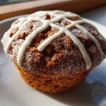 Close-up of a single, dark brown Gluten-Free Hot Cross Bun Muffin topped with white icing cross and sparkling sugar.