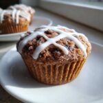 A close-up of one delicious Gluten-Free Hot Cross Bun Muffin topped with white cross icing on a white plate.