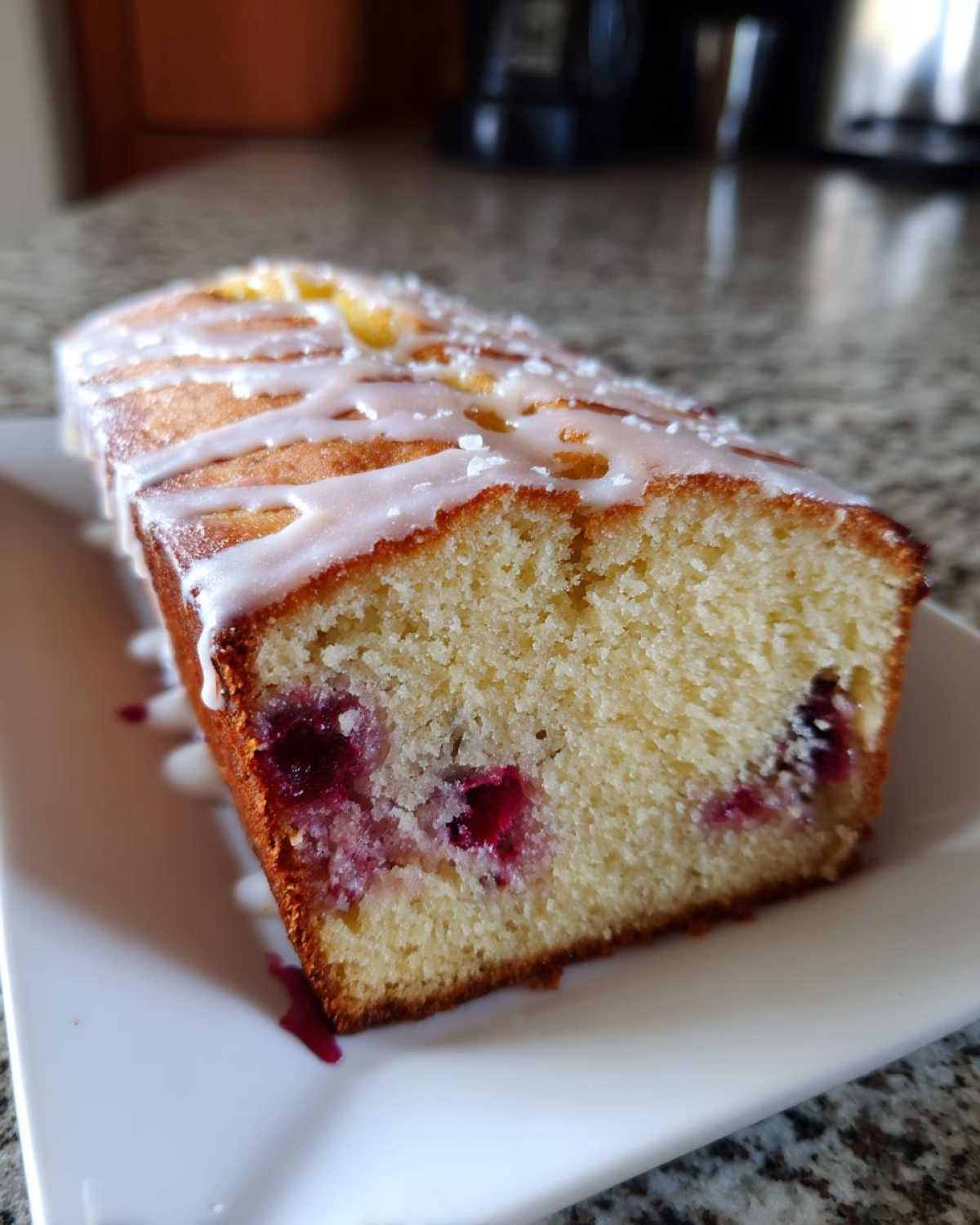 Close-up of a slice of Gluten-Free Lemon Berry Yogurt Cake drizzled with white icing and coarse sugar.