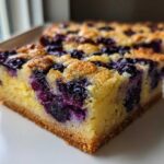 Close-up of a thick slice of Gluten-Free Lemon Blueberry Layer Bars showing a dense yellow cake base mixed with vibrant purple blueberries.