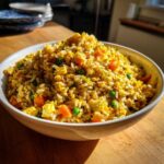 A generous serving of vibrant Gluten-Free Lemon Pepper Fried Rice with scrambled egg, peas, and carrots in a white bowl.