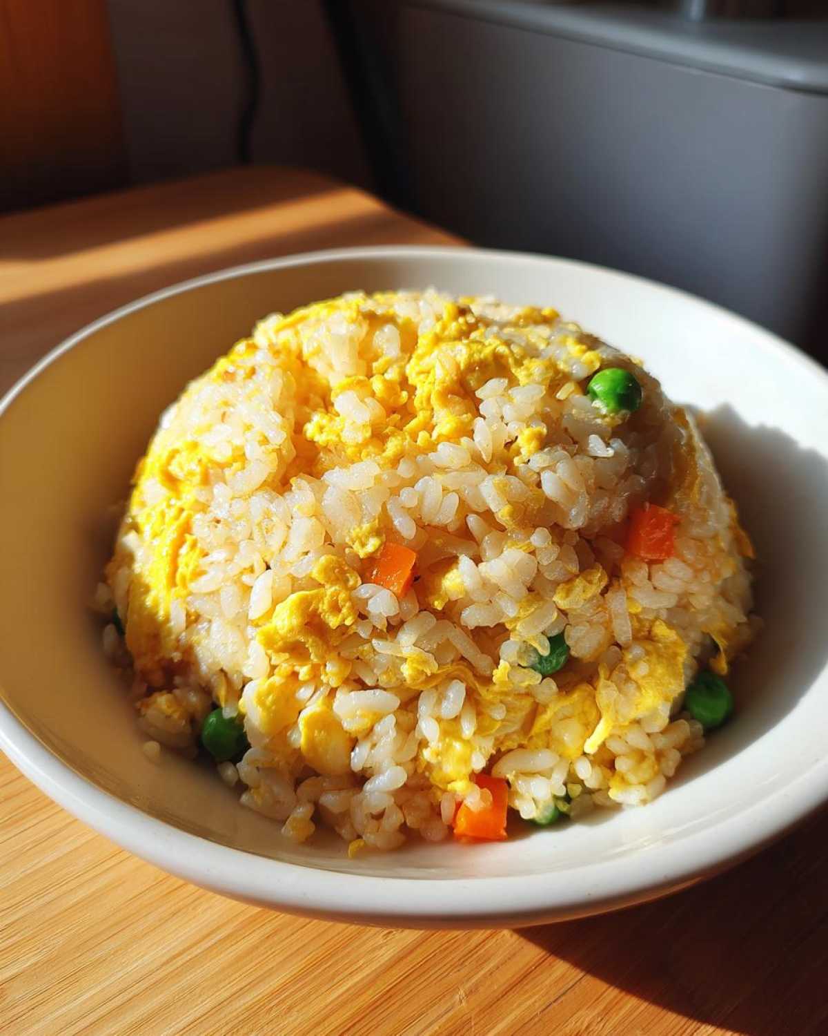 A bowl of perfectly formed Gluten-Free Lemon Pepper Fried Rice mixed with scrambled egg, peas, and diced carrots.