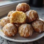 A stack of shiny, glazed Gluten-Free Lemon Poppy Seed Donut Holes on a white plate, one cut open showing the crumb.