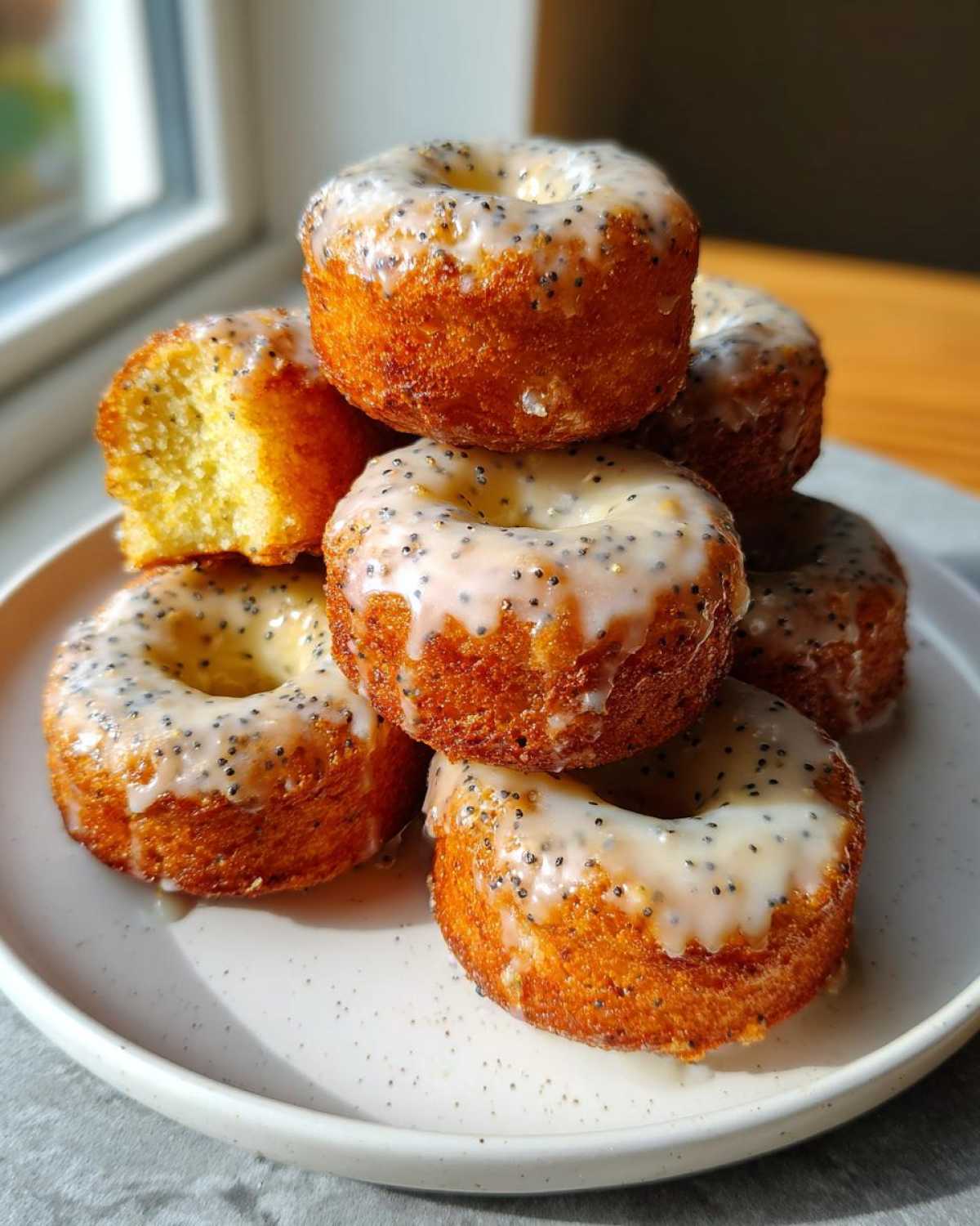 A stack of freshly glazed Gluten-Free Lemon Poppy Seed Donut Holes on a white plate, one is broken open showing the interior.