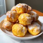 A stack of golden Gluten-Free Lemon Poppy Seed Donut Holes drizzled with a thick, white lemon glaze.