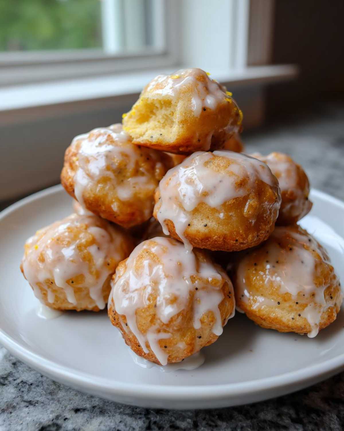 A stack of golden Gluten-Free Lemon Poppy Seed Donut Holes drizzled generously with white lemon glaze on a white plate.
