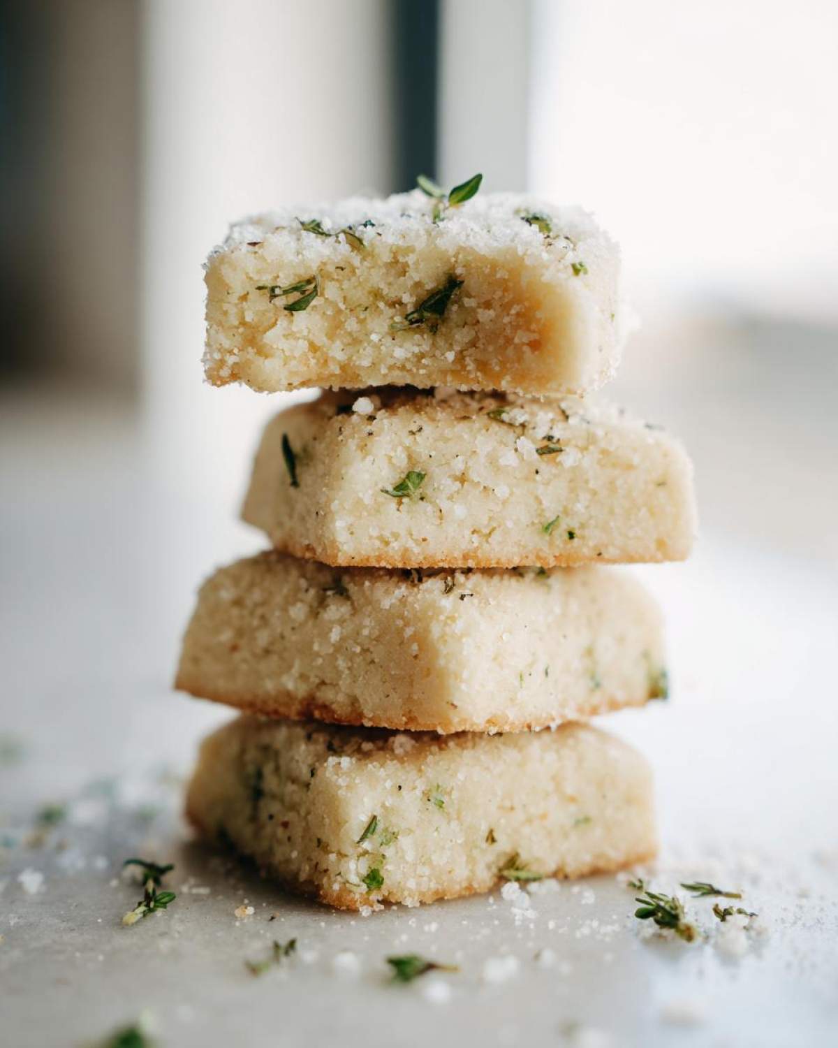 A vertical stack of four square Gluten-Free Lemon Thyme Shortbread Cookies dusted with sugar and fresh thyme.