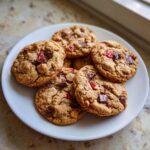 A white plate stacked with freshly baked Gluten-Free Strawberry Chocolate Chip Cookies featuring visible chunks of chocolate and red strawberry pieces.