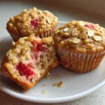 Three Gluten-Free Strawberry Oat Muffins on a white plate, one broken open showing moist interior and strawberries.