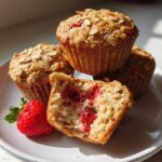 Close-up of Gluten-Free Strawberry Oat Muffins, one cut open showing the moist interior and bright red strawberries.