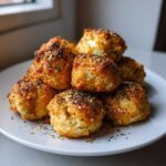 A stack of golden-brown High-Protein Cottage Cheese Bagel Bites topped with everything bagel seasoning on a white plate.