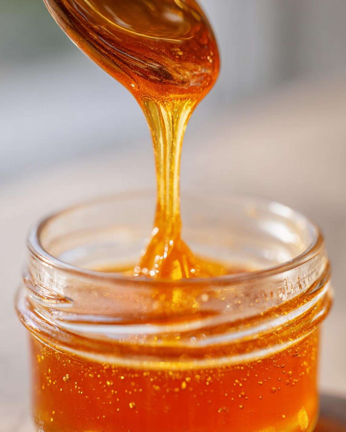 Close-up of thick, amber honey being drizzled from a spoon into a small glass jar for Copycat Apple Cider Vinaigrette.