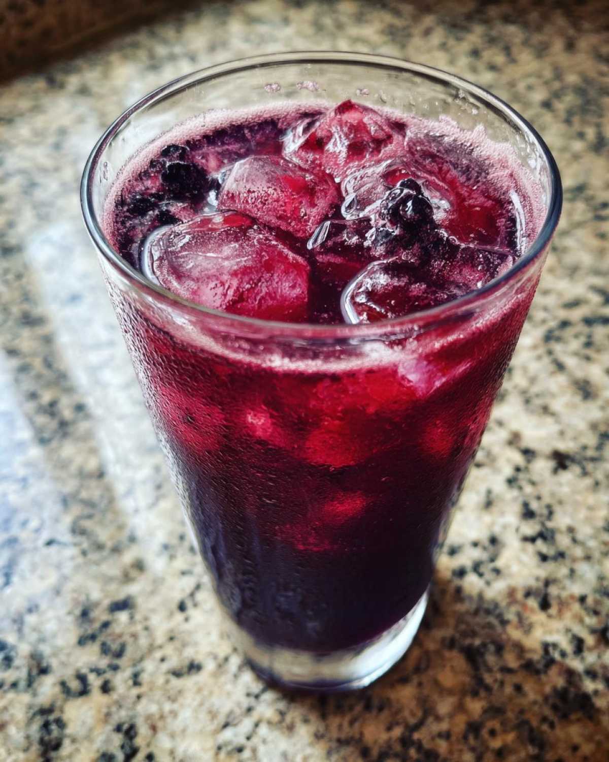 Close-up of a tall glass filled with deep red Iced Blackberry Sage Tea and ice cubes.