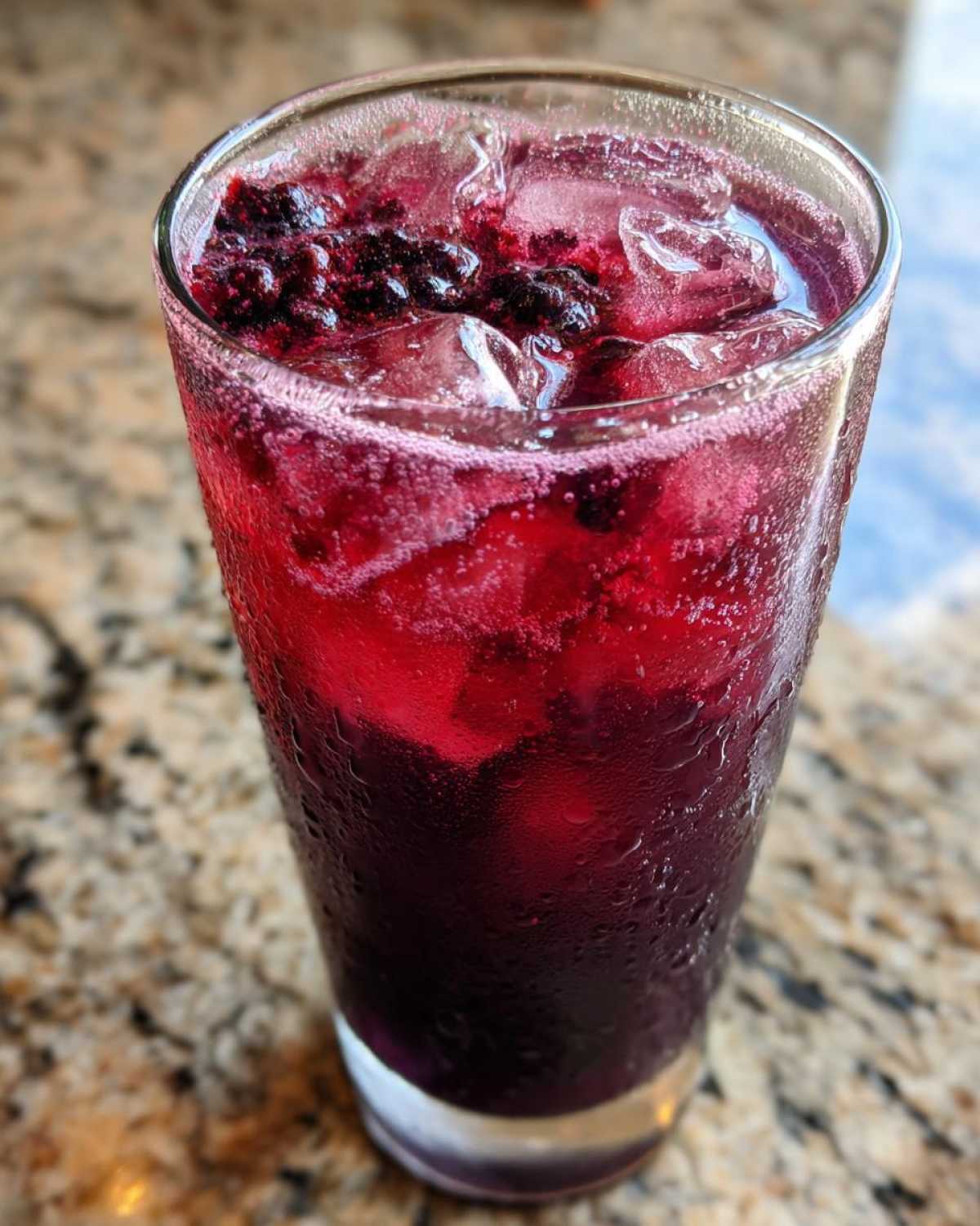 Close-up of a tall glass filled with Iced Blackberry Sage Tea, ice, and fresh blackberries.