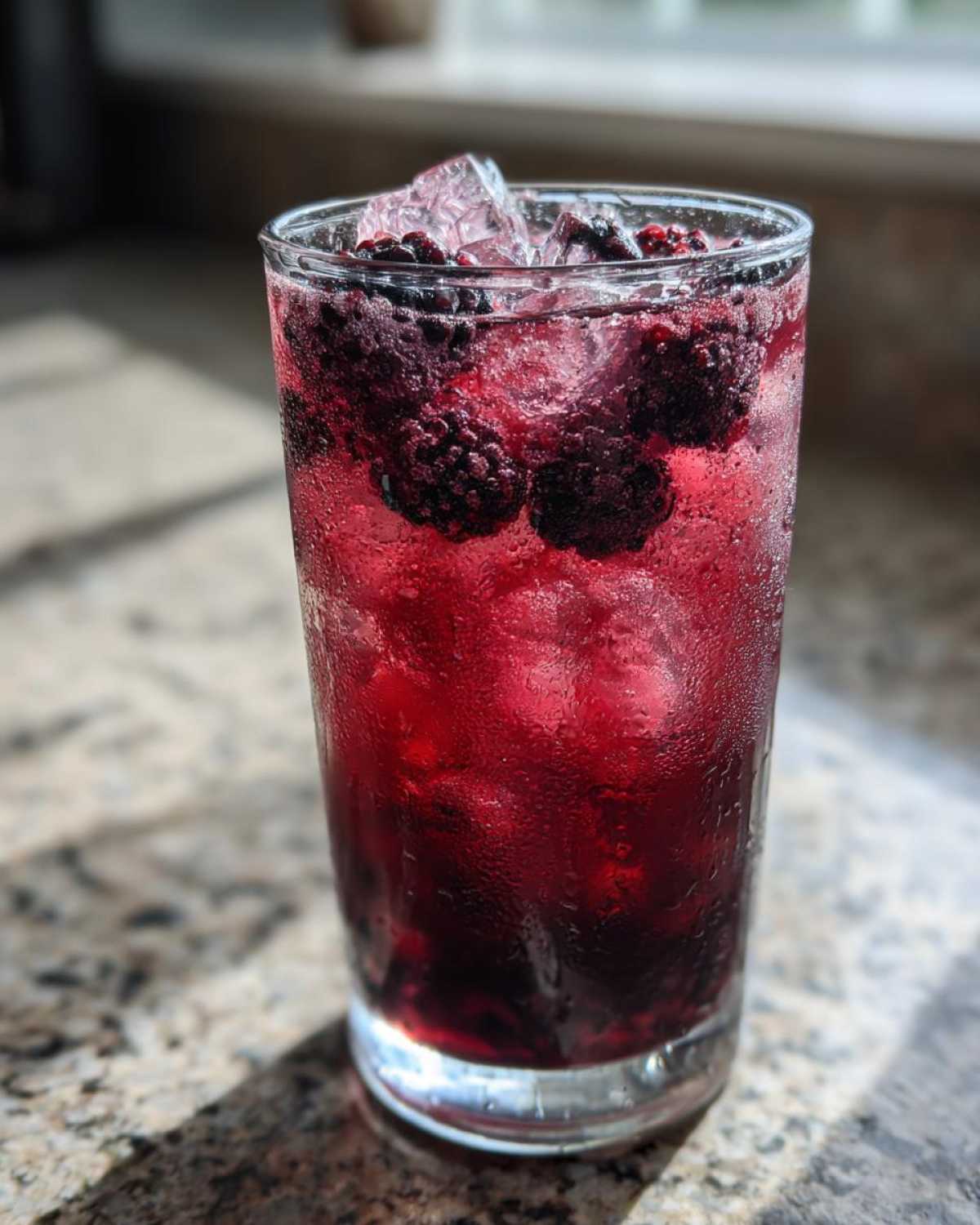 A tall, sweating glass filled with Iced Blackberry Sage Tea, ice cubes, and whole fresh blackberries.