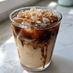 A tall glass showing the beautiful layering of dark espresso mixing with creamy oat milk in an Iced Honey Vanilla Latte with Oat Milk.