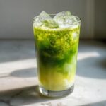 A tall glass of Iced Matcha Pineapple Refresher showing vibrant green matcha layered over a lighter base, filled with ice.