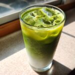 A tall glass of layered Iced Matcha Pineapple Refresher with ice cubes, sitting in bright sunlight.