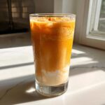 A tall glass filled with a vibrant orange Iced Orange Creamsicle Smoothie, showing separation between the orange layer and the creamy white base.