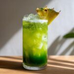 A vibrant green Iced Pineapple Matcha Spritz served over ice in a tall glass, garnished with a fresh pineapple wedge.