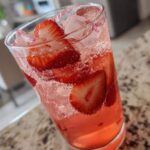 Close-up of a tall glass filled with Iced Strawberry Hibiscus Tea Lemonade, ice, and fresh strawberry slices.