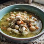 Close-up of a bowl of Instant Pot Chicken Pozole Verde featuring shredded chicken, hominy, and carrots in a green broth.
