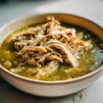 Close-up of a bowl filled with vibrant green broth and a generous topping of shredded chicken from Instant Pot Chicken Pozole Verde.