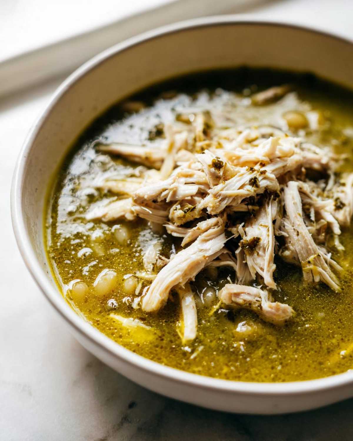 Close-up of a bowl of Instant Pot Chicken Pozole Verde topped with a generous helping of shredded chicken.