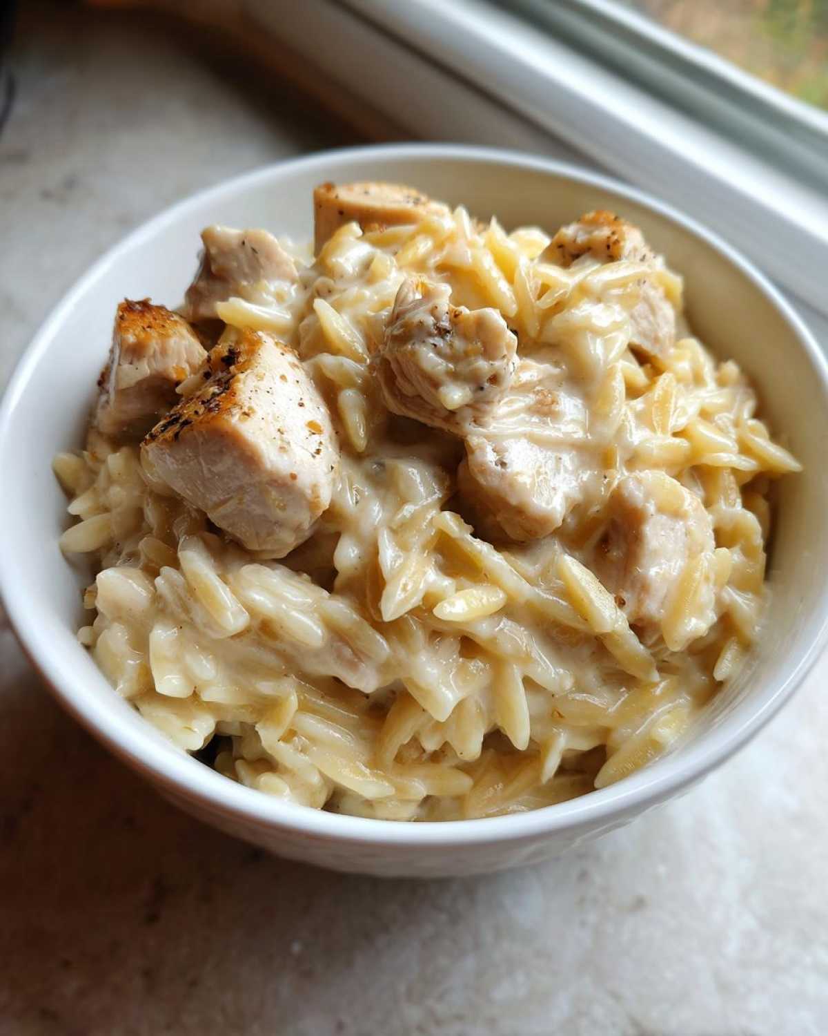 Close-up of a white bowl filled with Instant Pot Creamy Chicken and Orzo, featuring tender chicken pieces in a rich sauce.