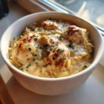 A white bowl filled with Instant Pot Creamy Chicken and Orzo, topped with melted cheese and fresh parsley.