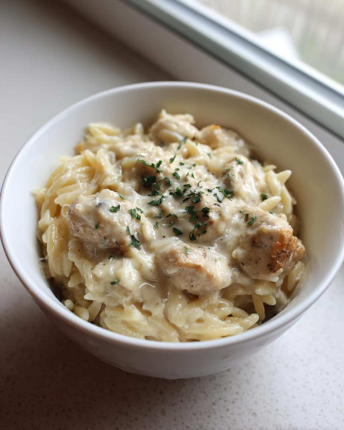 A close-up of Instant Pot Creamy Chicken and Orzo topped with fresh parsley in a white bowl.