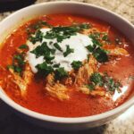 Close-up of a bowl of Instant Pot Creamy Chicken Enchilada Soup topped with sour cream and fresh cilantro.