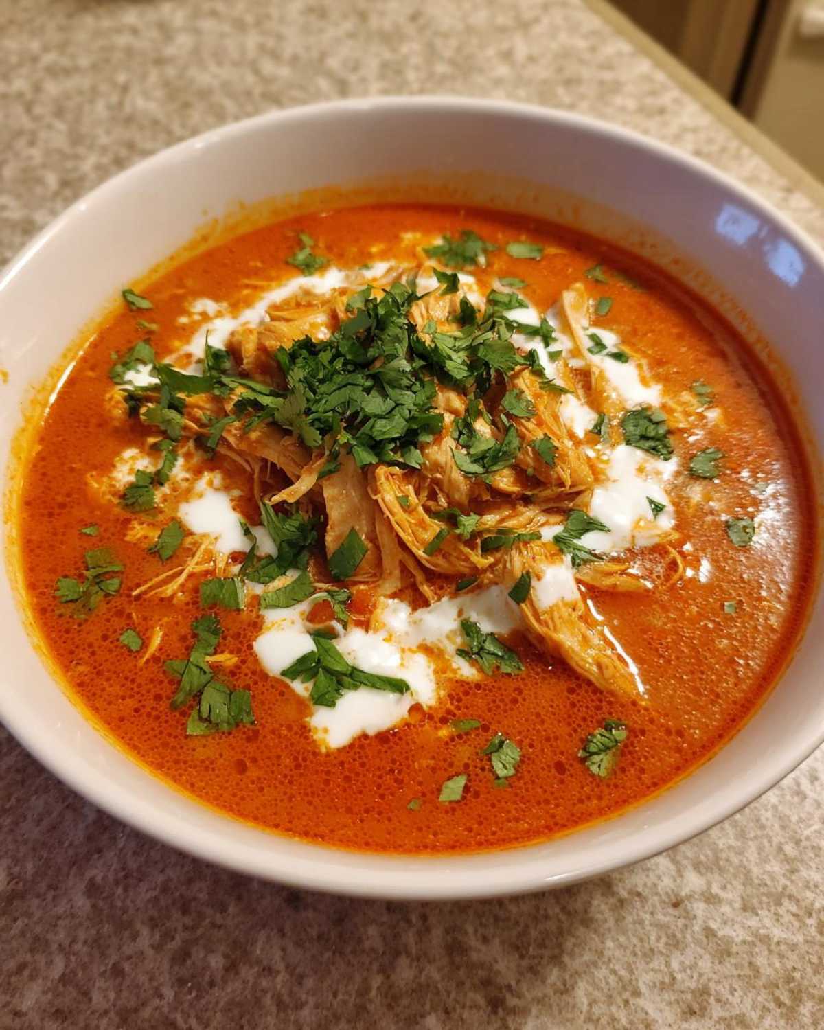 Close-up of a bowl of vibrant orange Instant Pot Creamy Chicken Enchilada Soup topped with shredded chicken, sour cream, and cilantro.
