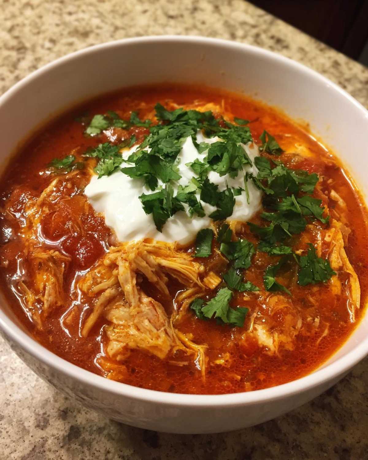 Close-up of a bowl of Instant Pot Creamy Chicken Enchilada Soup topped with sour cream and fresh cilantro.