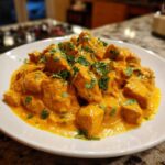A close-up of rich, orange Instant Pot Creamy Coconut Chicken Curry served on a white plate and garnished with fresh cilantro.