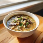 A white bowl filled with rich Instant Pot Creamy Mushroom Barley Soup, topped with sliced mushrooms and fresh parsley.