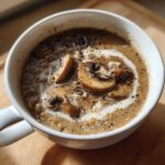 Close-up of a white mug filled with rich Instant Pot Creamy Mushroom Barley Soup, garnished with sliced mushrooms and a cream swirl.