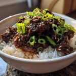 Close-up of a white bowl filled with white rice topped with saucy Instant Pot Korean Beef and green onions.