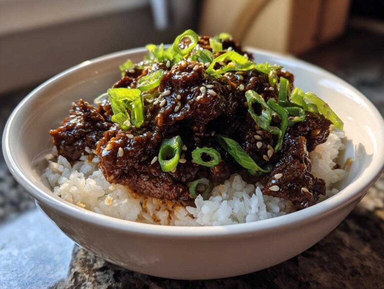Close-up of a white bowl filled with white rice topped with saucy Instant Pot Korean Beef and green onions.