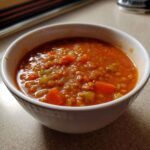 Close-up of a white bowl filled with thick Instant Pot Tomato Lentil Soup, showing lentils, carrots, and celery.