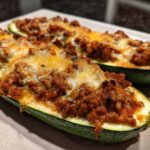 Two halves of Keto Cheesy Taco Stuffed Zucchini Boats, generously filled with seasoned ground meat and melted cheese.