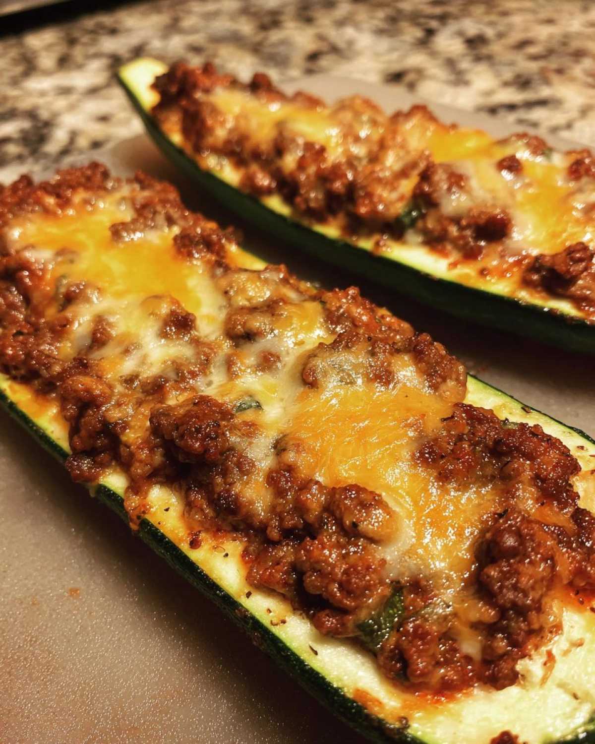 Two baked Keto Cheesy Taco Stuffed Zucchini Boats topped with seasoned ground meat and melted cheddar cheese.