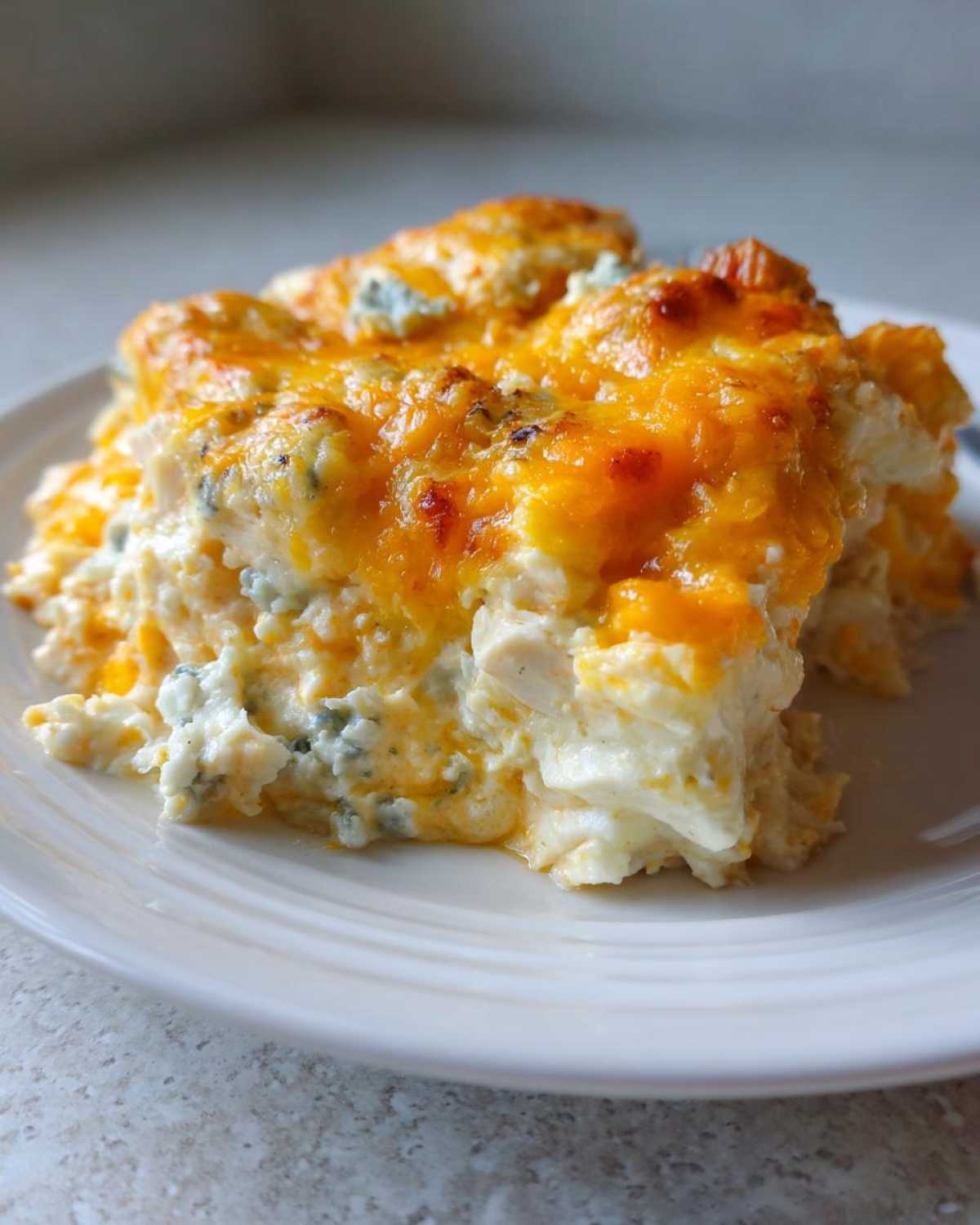A close-up serving of Keto Creamy Buffalo Chicken Casserole topped with melted cheddar and blue cheese.